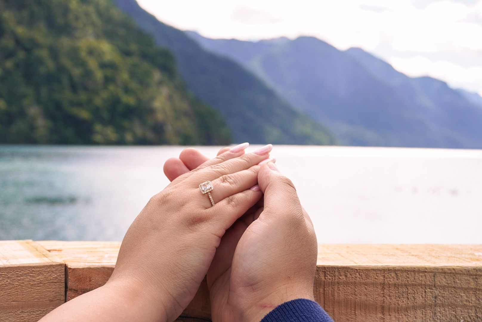 Manos de Benjamin y Kiara entrelazadas con el anillo de compromiso, junto al lago